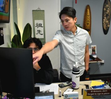 Photo of two people at a computer, one pointing to the monitor.