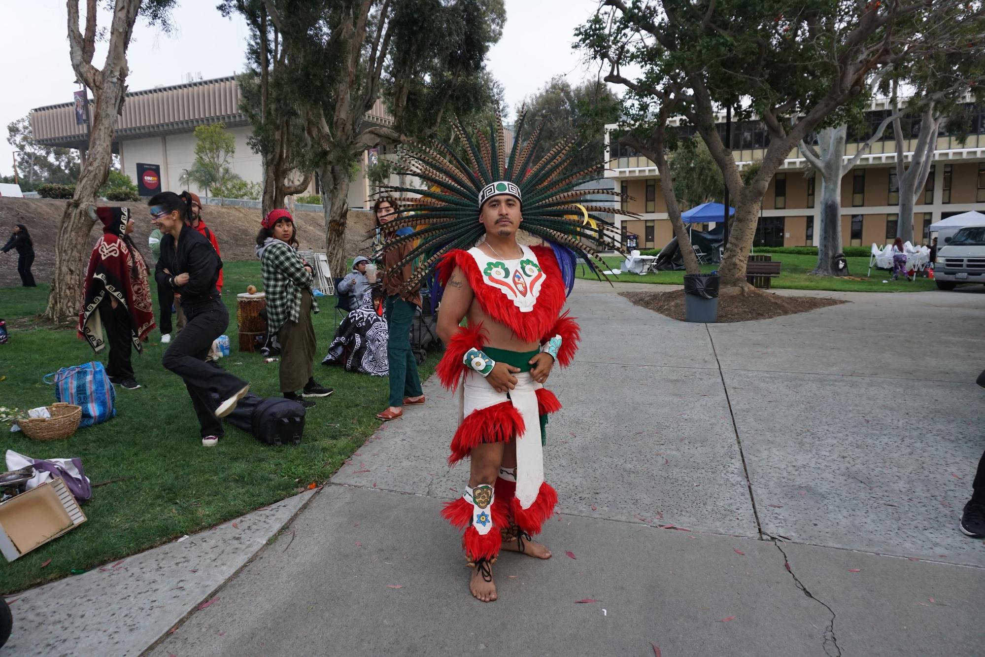 Photo of person standing on a sidewalk with headdress and outfit.
