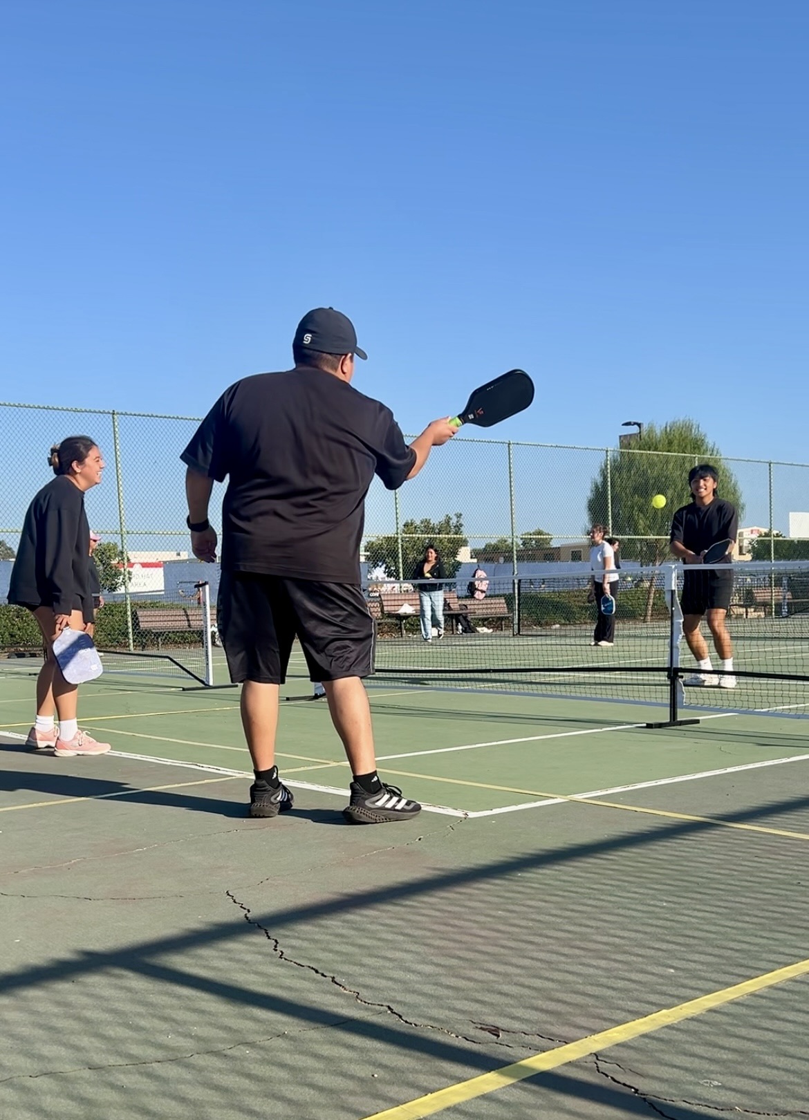 Photo of three people dressed in black playing pickleball with paddles.