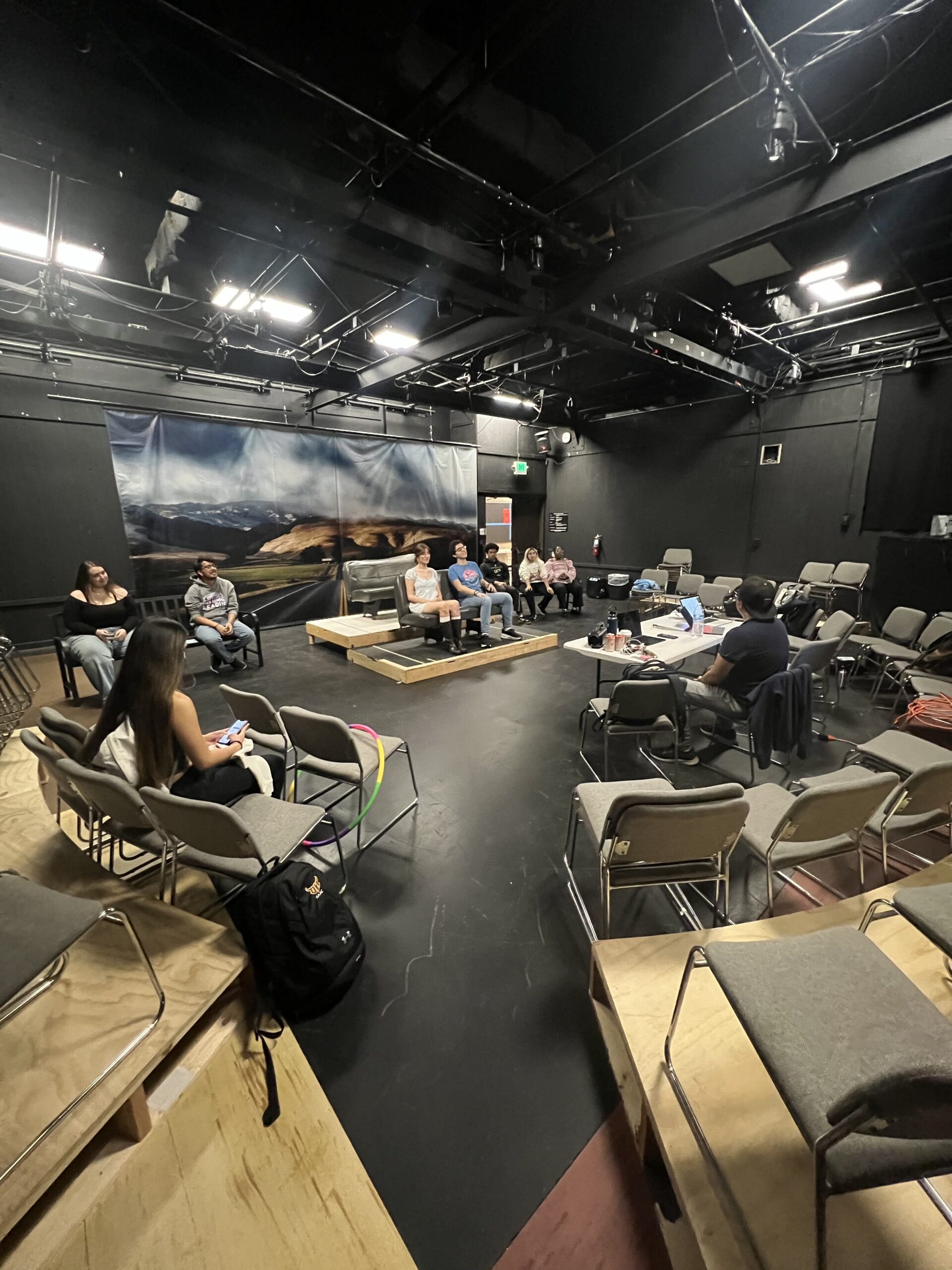 Fish eye shot of a black box theater with people seated around the stage and rehearsing